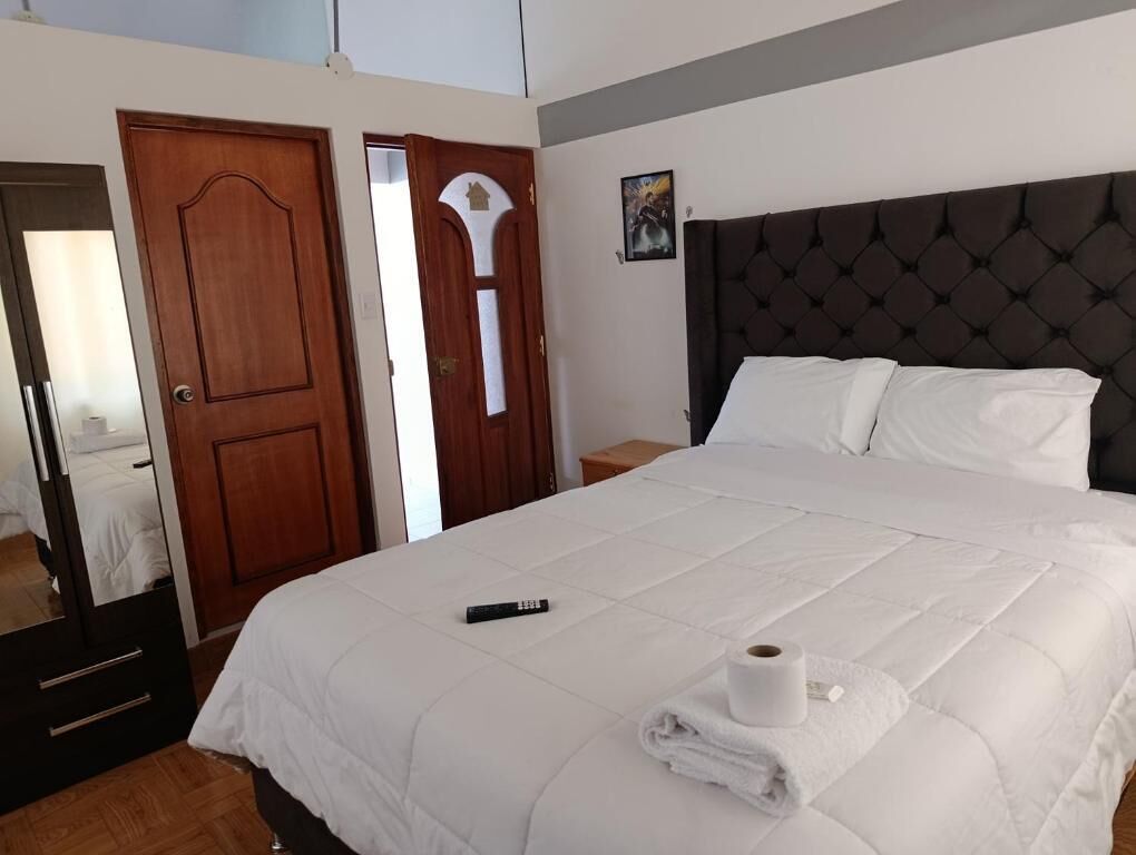 Habitación de hotel con una cama grande, una puerta de madera, un espejo y un cuadro enmarcado en la pared.