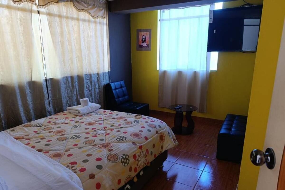 Una habitación de hotel con una cama, una silla, una mesita y un banco.