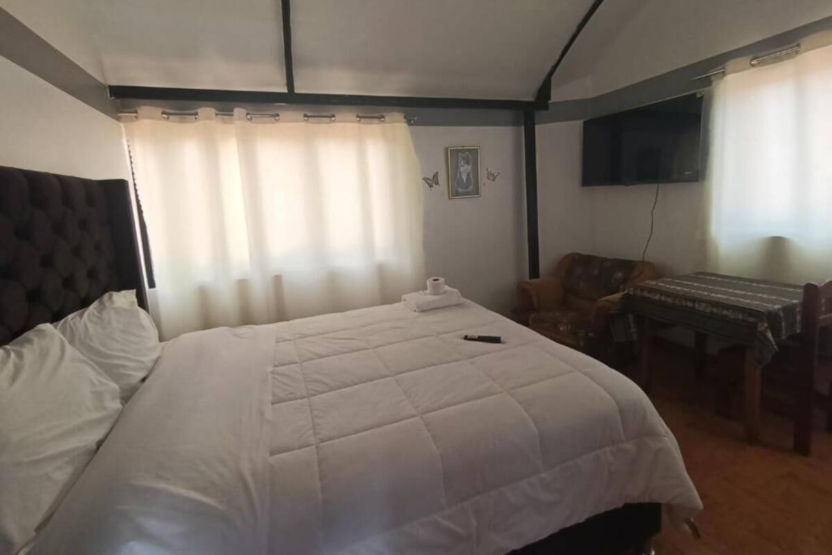 Habitación de hotel con cama, escritorio, silla, televisor y ventana con cortinas.
