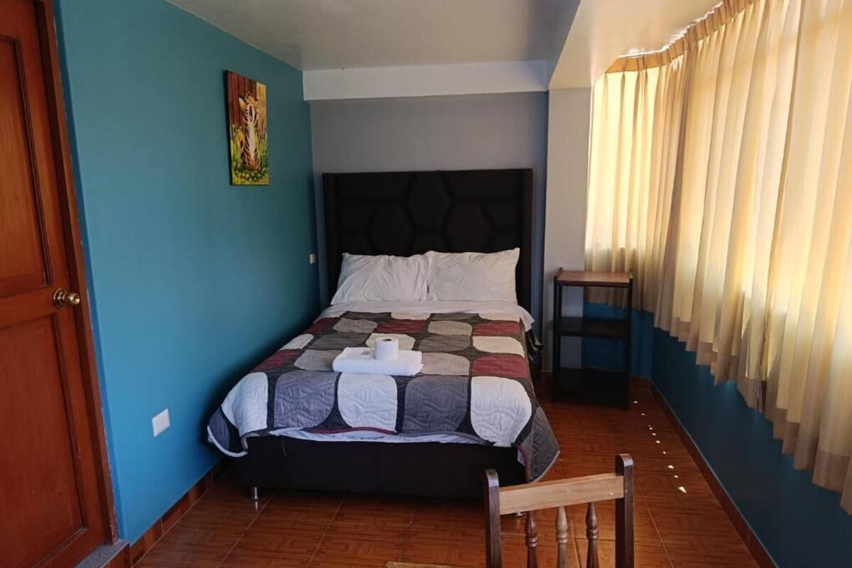 Un dormitorio con una cama, una silla, una mesita, una puerta y una cortina.