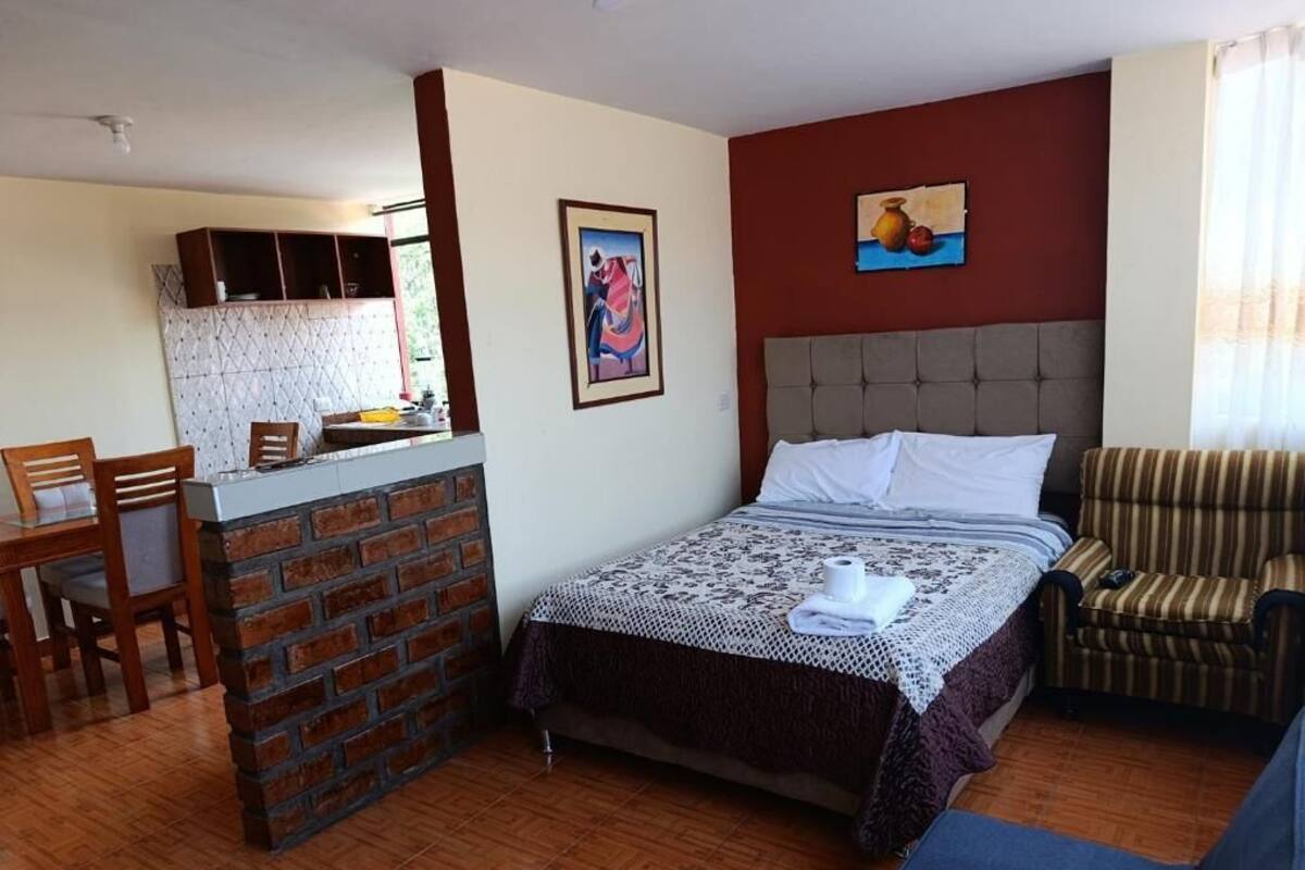 Una habitación con cama, una silla, una mesita y una kitchenette.
