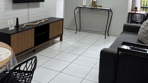 Una sala de estar con televisor de pantalla plana, un sofá, una mesa de comedor con sillas y una mesita auxiliar con un florero.