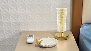 Una mesita de noche con una lámpara, un control remoto y una concha decorativa.