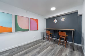 Une pièce avec un mur de couleur sombre, un bureau en bois, deux chaises en bois et trois tableaux abstraits.