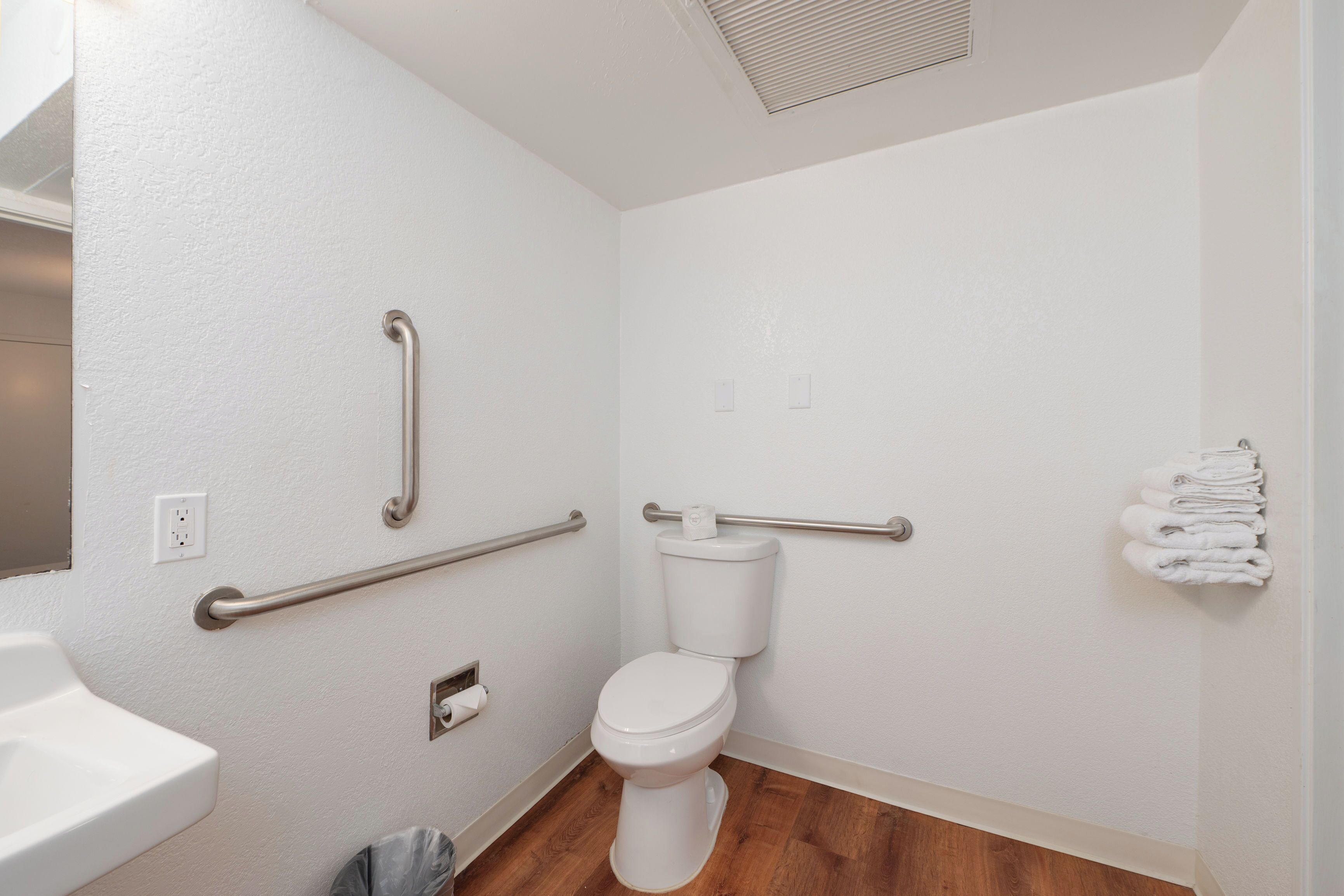 Ein Badezimmer mit Toilette, Haltegriffen, Waschbecken und Handtuchhalter.