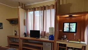 Una habitación con cama, escritorio con computadora, kitchenette pequeña y ventilador de techo.