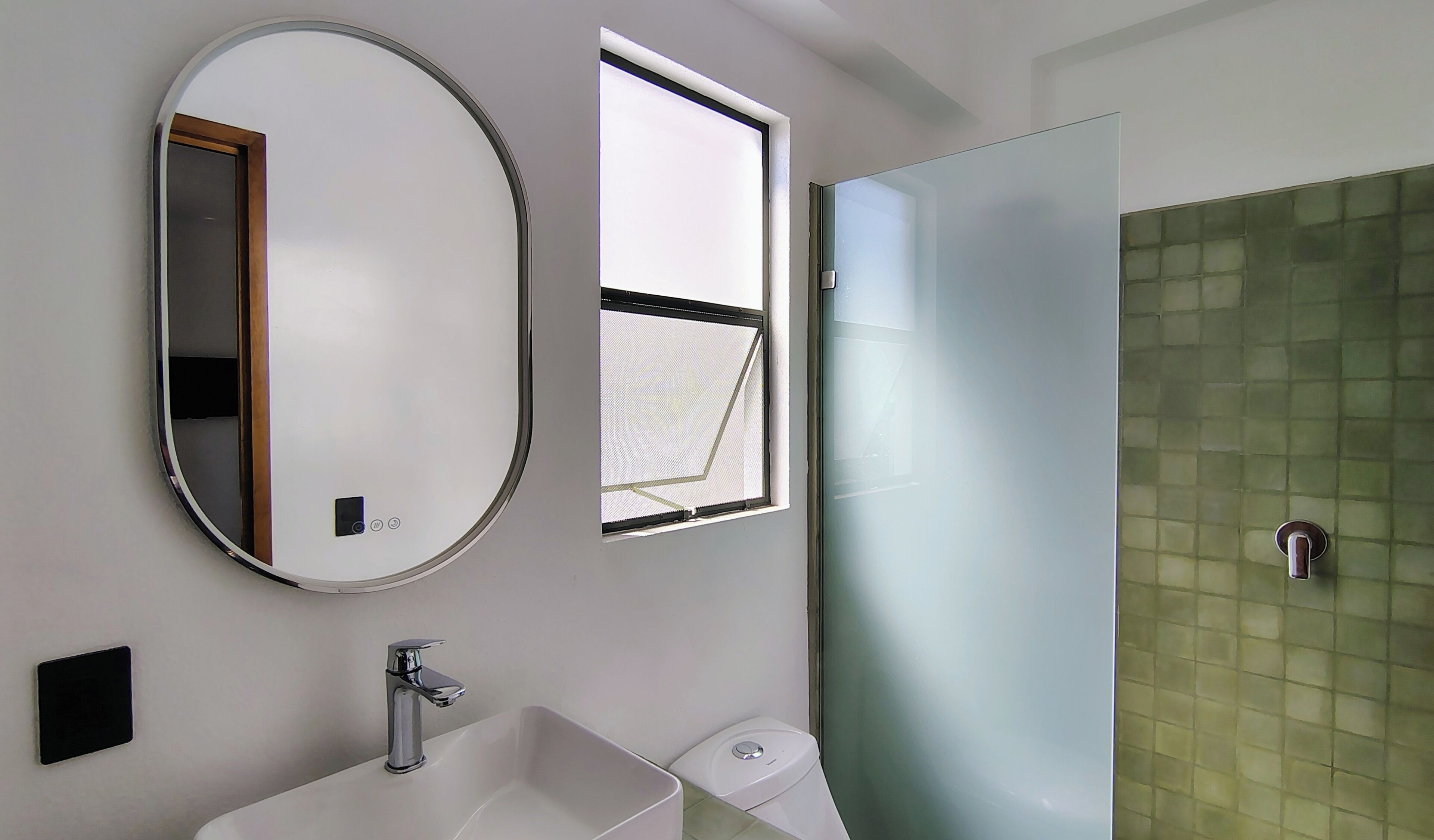 A bathroom with a round mirror, a window, a sink, and a toilet.