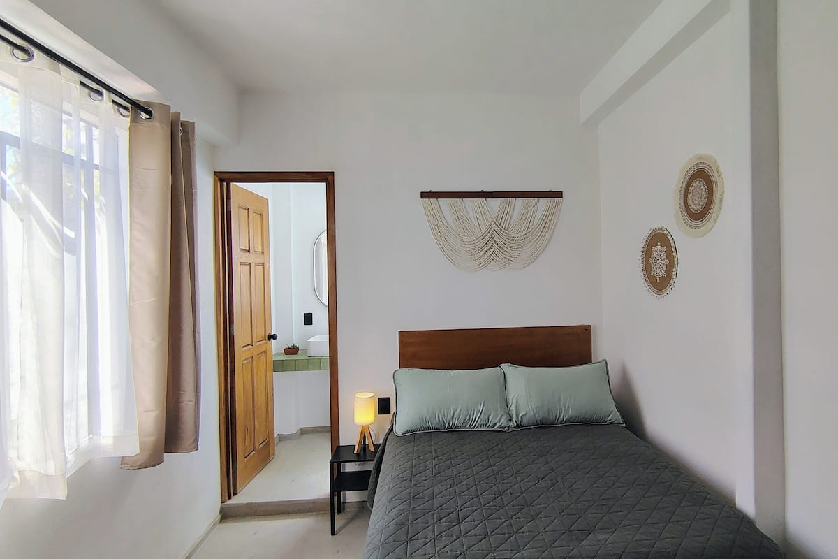 Un dormitorio con una cama, una mesita de noche con lámpara, una puerta de madera y vistas al baño.