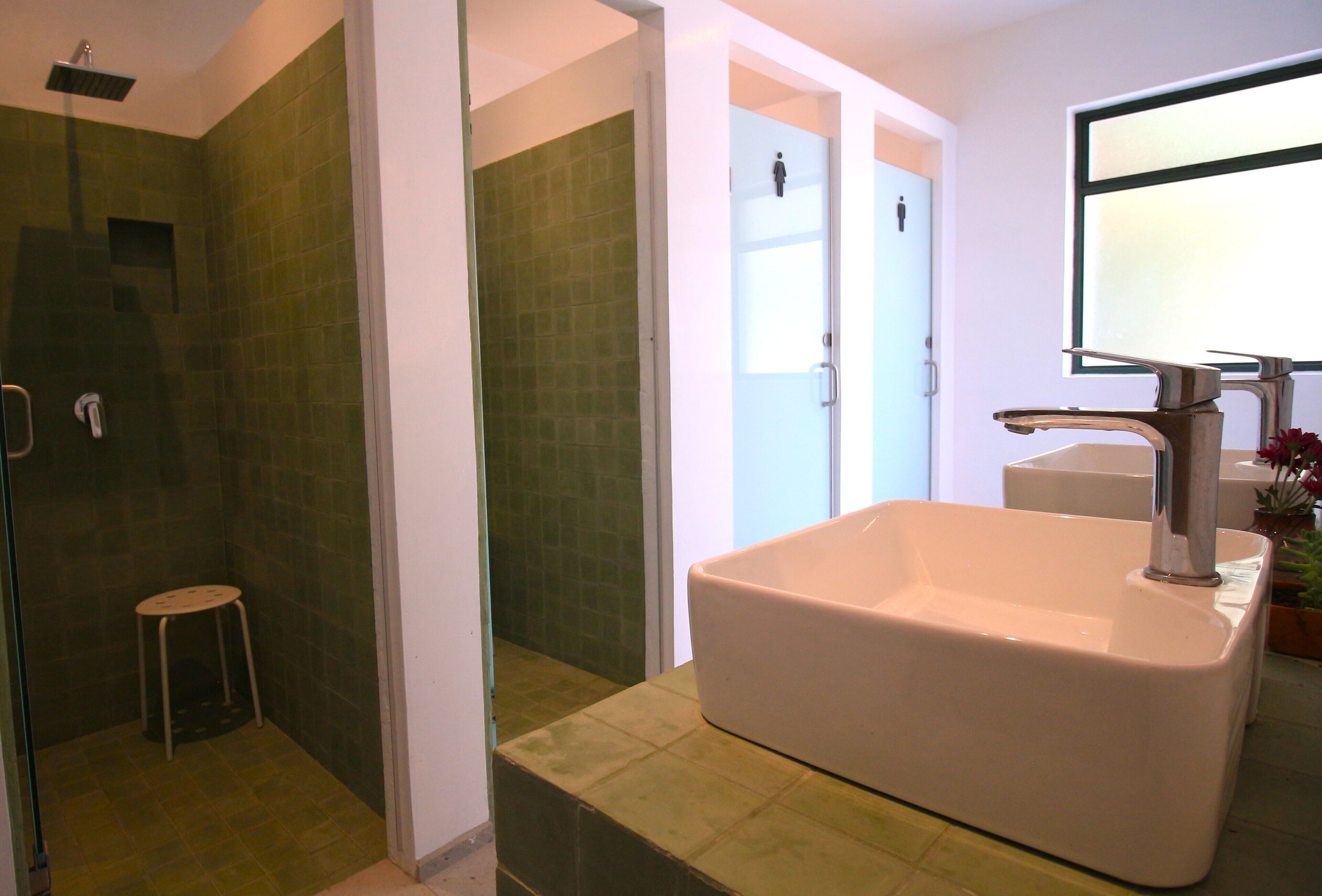 A bathroom with a large white sink, a shower area, and a small stool.