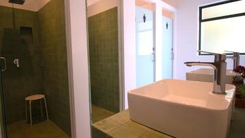 A bathroom with a large white sink, a shower area, and a small stool.