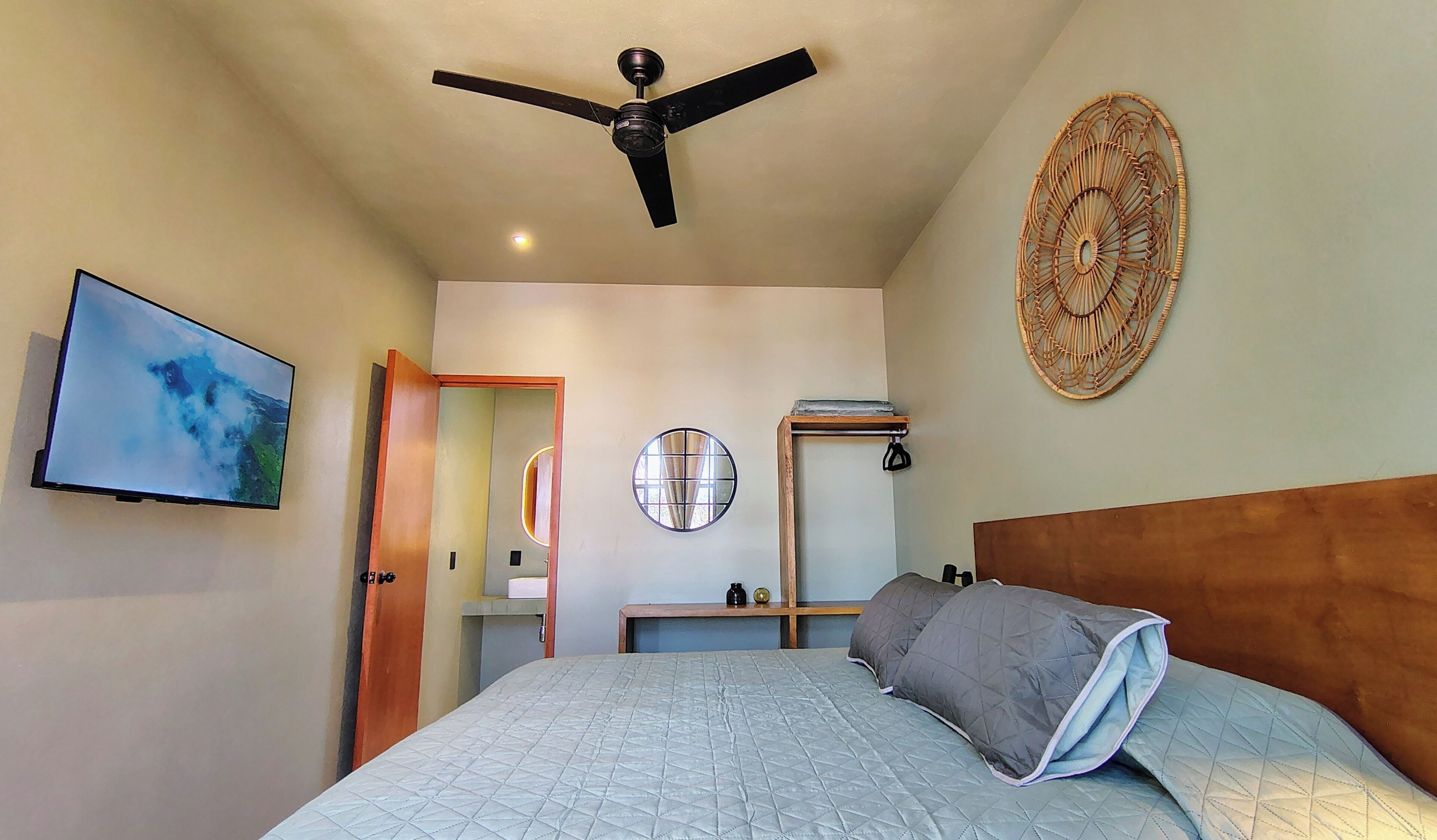 A bedroom with a bed, a ceiling fan, a TV, a wall-mounted mirror, and a decorative wall piece.