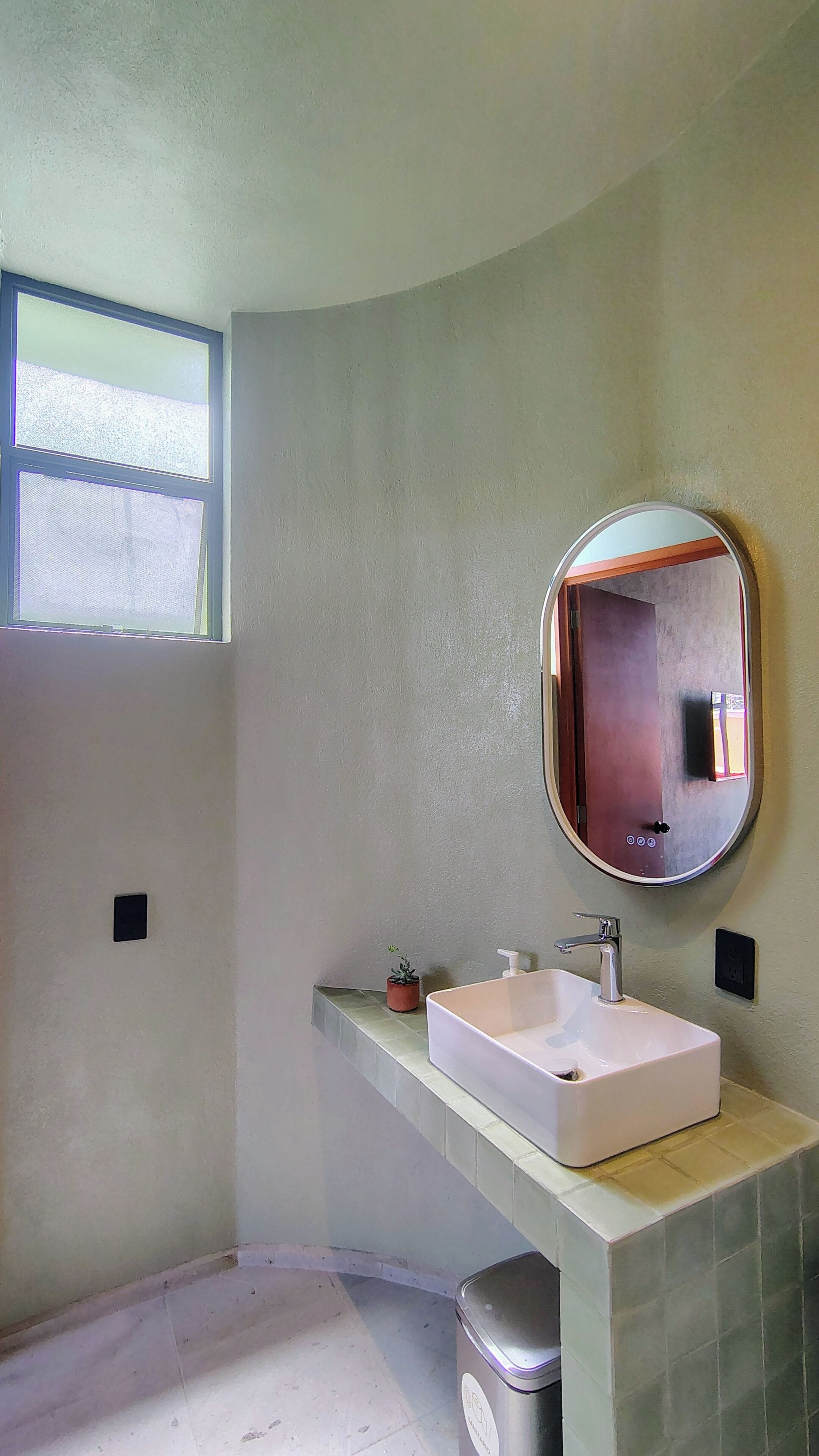 A bathroom with a white sink, a round mirror, and a window.