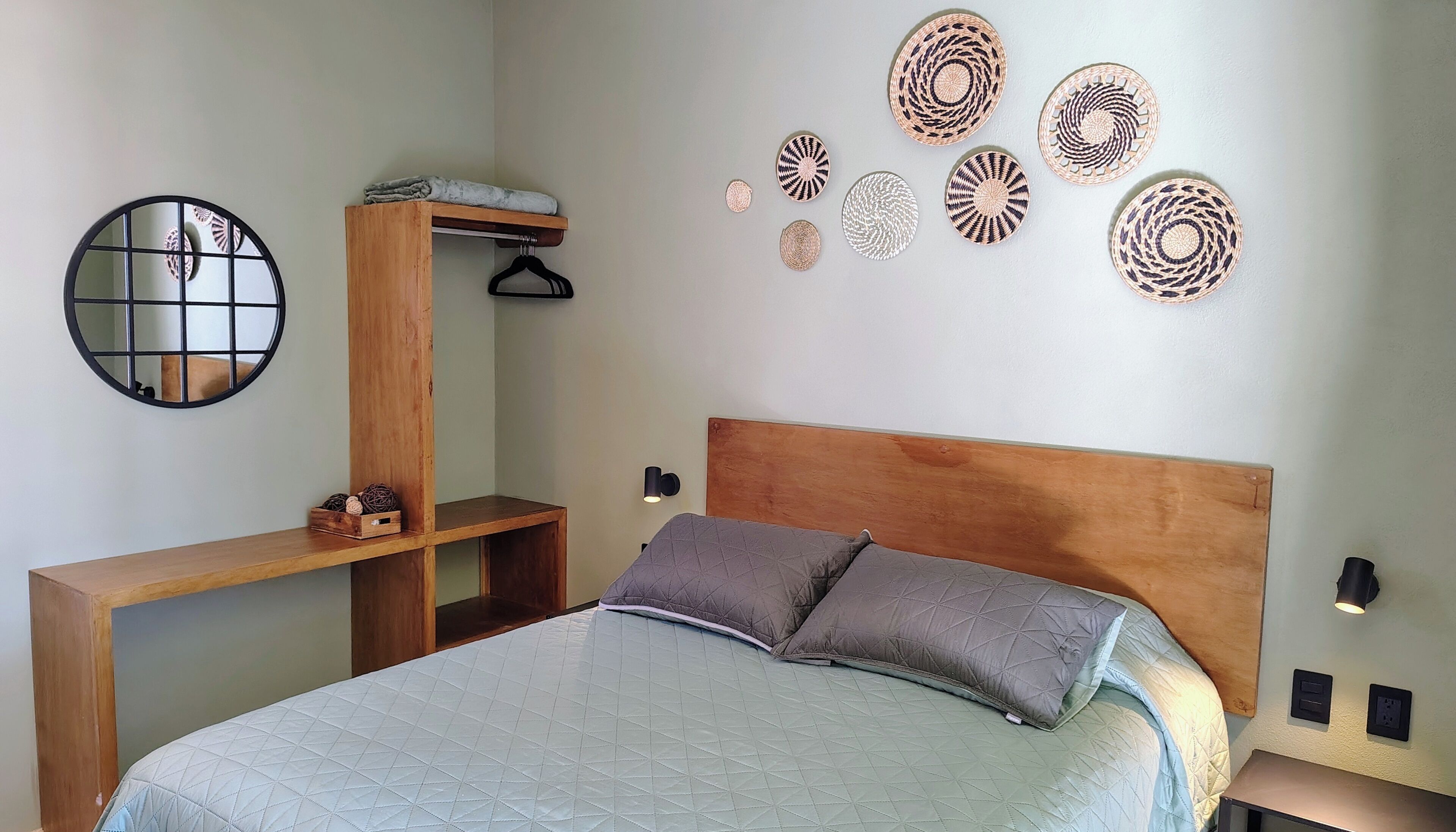 A bedroom with a bed, a wooden headboard, a bedside table, a mirror, and wall decor.