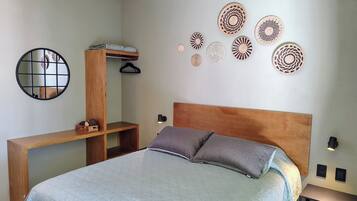 A bedroom with a bed, a wooden headboard, a bedside table, a mirror, and wall decor.