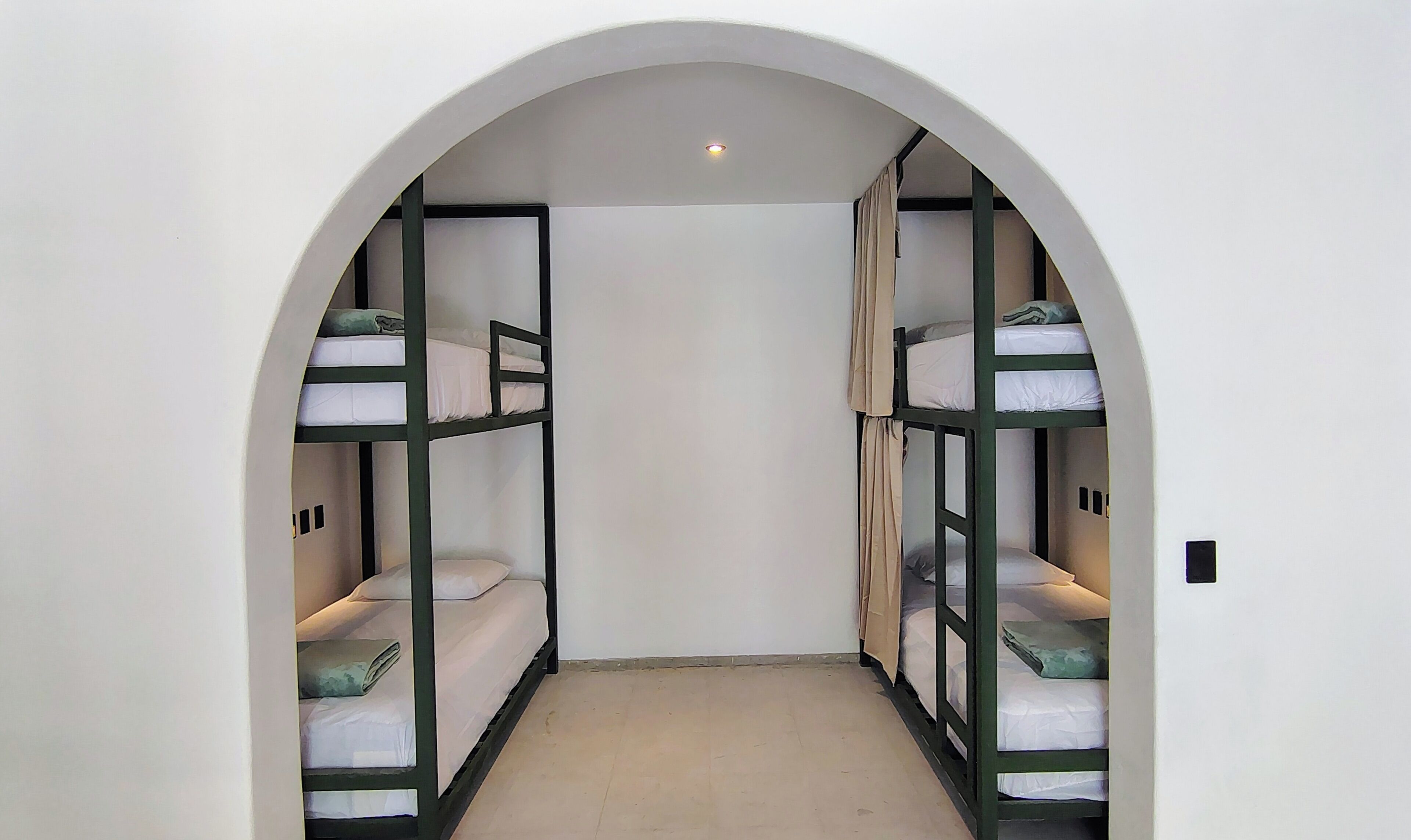 A narrow hallway with bunk beds on either side, an arched ceiling, and a recessed light at the end.