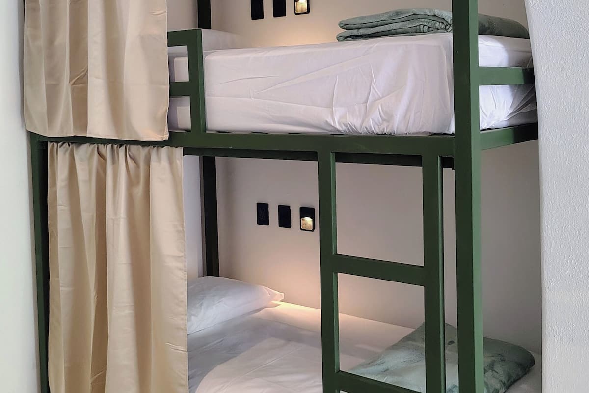 Una cama litera con cortina, una lámpara fijada a la pared y un estante pequeño.