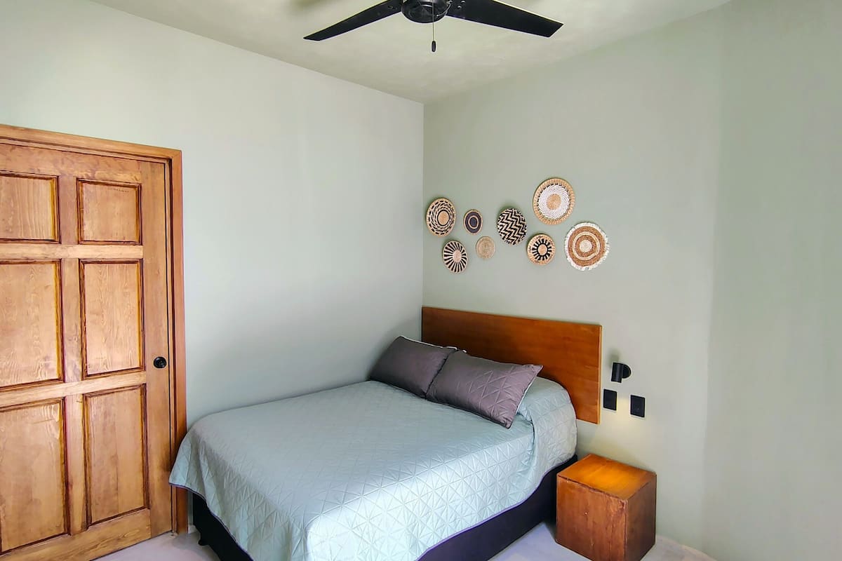 Un dormitorio con cama, una puerta de madera, ventilador de techo y decoración en las paredes.