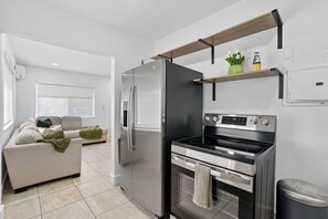 Eine moderne Küche mit Kühlschrank, Backofen und integriertem Mikrowellenherd. Im angrenzenden Wohnbereich befindet sich eine Couch und ein Fenster.