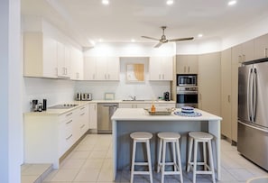 Eine moderne Küche mit weißen Schränken, einer zentralen Kochinsel mit Hockern, einer Mikrowelle, einem Backofen und einem Kühlschrank.