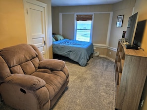Un dormitorio con cama, una silla, cómoda y ventana con vistas.