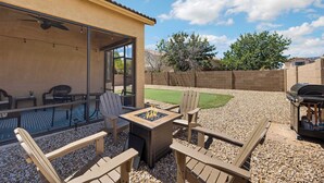 Un patio trasero con un brasero, mobiliario exterior, una parrilla y vistas a un campo verde.