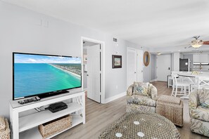 Ein Wohnzimmer mit Fernseher, weißen Möbeln und Blick auf den Ozean.