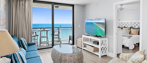 Una sala de estar con un televisor grande, una mesa redonda de centro, un sofá y un balcón con vista al océano.