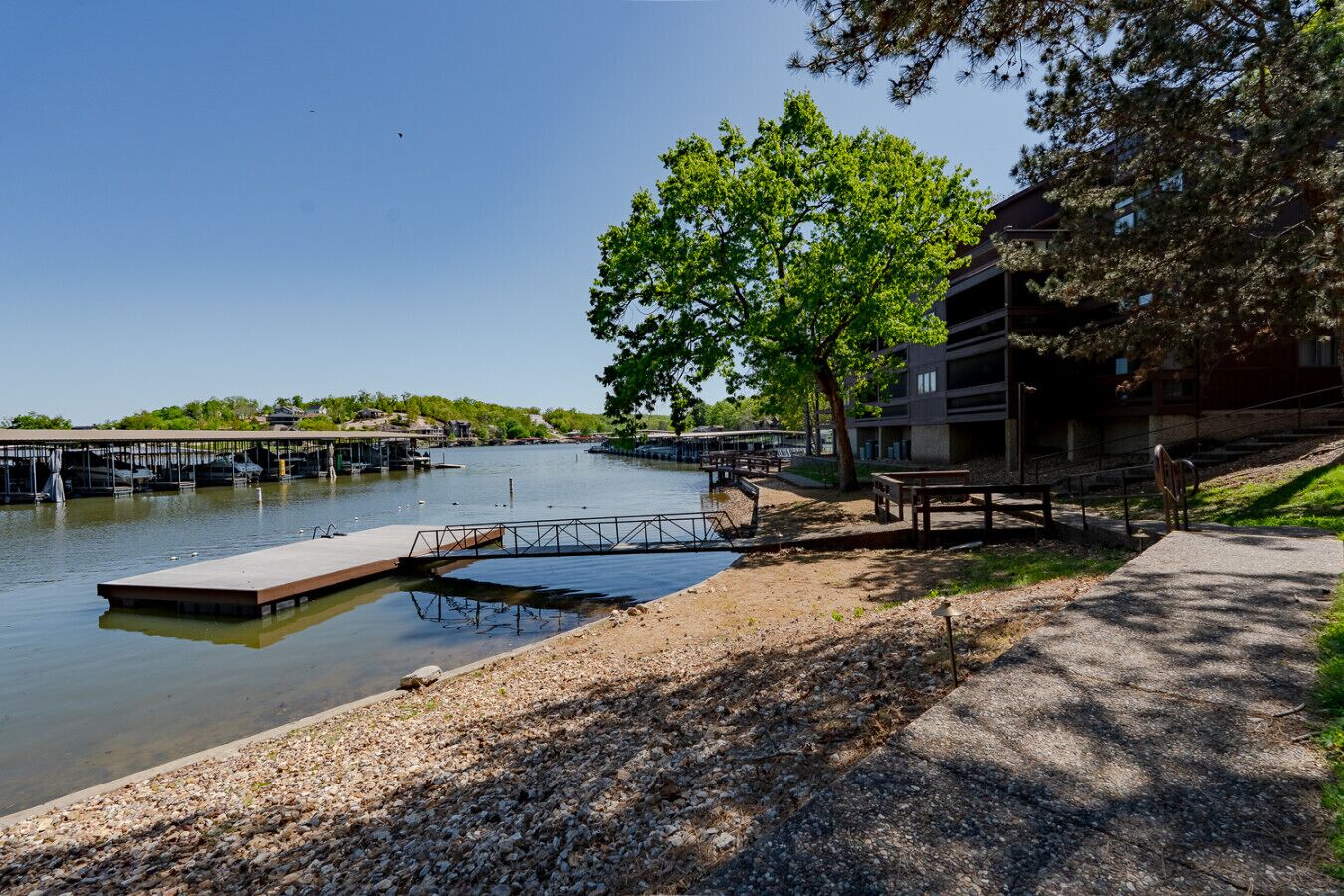 A riverside dock with a wooden platform, a pedestrian path, and a building with a flat roof.
