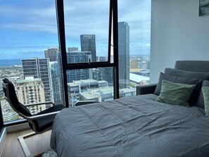 Une chambre avec une grande fenêtre, un lit, une chaise et une vue sur les immeubles de la ville.