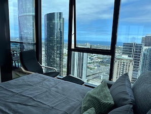 Une chambre d’hôtel située dans un immeuble de grande hauteur, dotée d’une grande fenêtre donnant sur la ville, d’un lit, d’une chaise et d’une petite table.