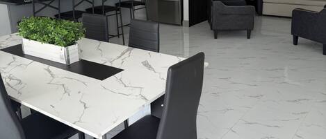 A modern kitchen with a marble countertop, a built-in refrigerator, and a dining area with a white table and black chairs.