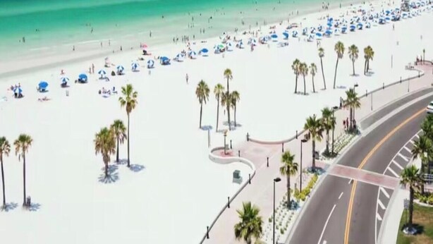 Una spiaggia con palme, ombrelloni e una strada.