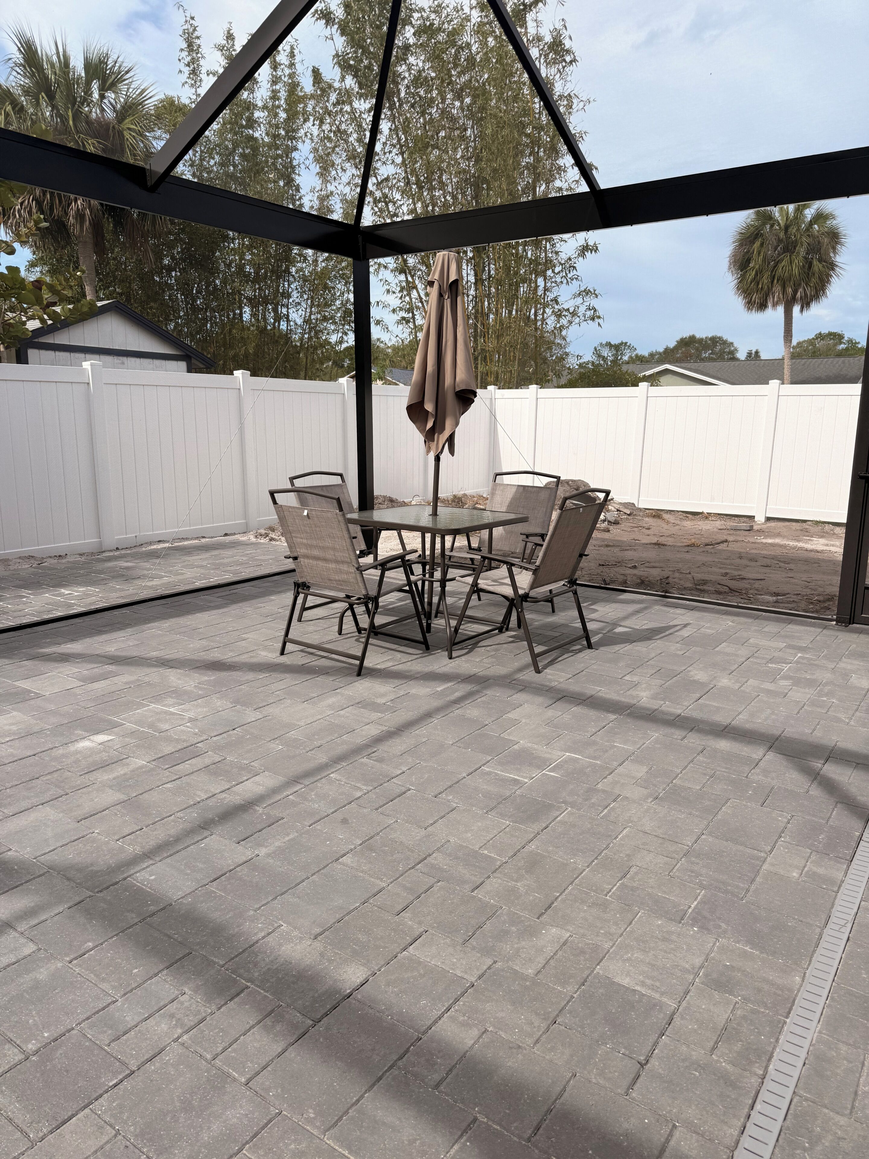 Une terrasse couverte avec une table et des chaises, une pergola et, au fond, une clôture blanche.