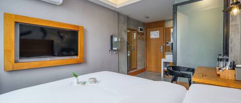 A hotel room with a bed, a desk, a chair, a mirror, and an air conditioning unit.