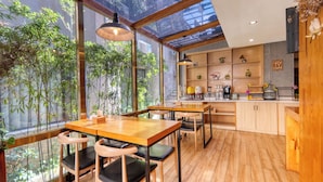 A modern kitchen with wooden cabinets, a dining area with a table and chairs, and large windows with a view of greenery. - Gongxili - Chujian Hotel (Kunming)