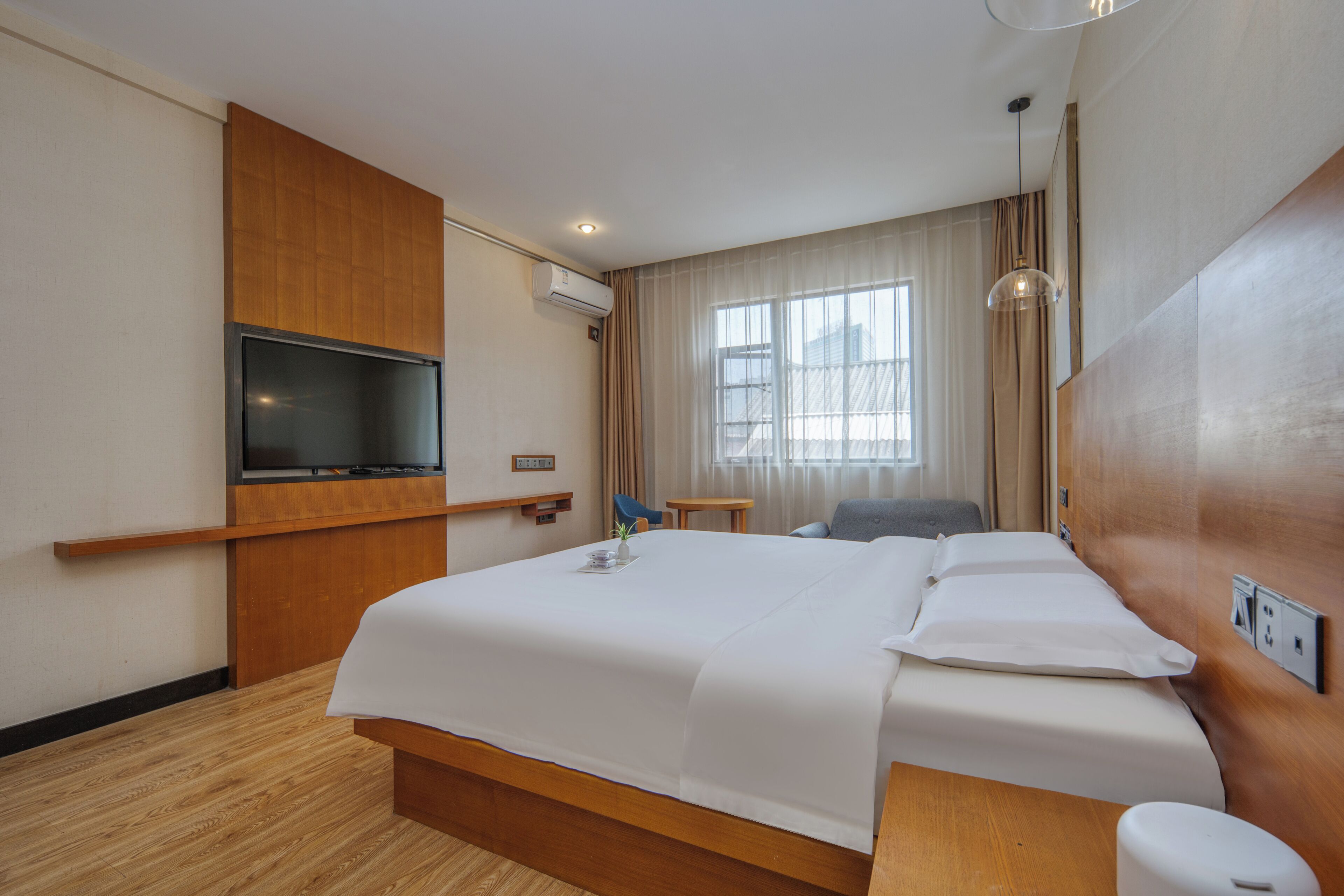 Hotelkamer met een bed, televisie, bureau, stoel, raam met gordijnen en een houten wandpaneel.