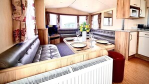 A compact RV interior with a dining area, seating, kitchenette, and a view of the outdoors. - Sea Views 2 Bed - Sleeps 6 - Pets - Parking - Wifi (Longmanhill)