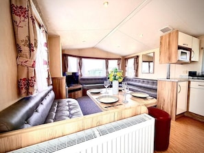 A compact RV interior with a dining area, seating, kitchenette, and a view of the outdoors.