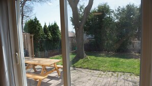 A patio with a wooden table and chairs, a fenced yard, and a tree. - Cozy Retro Suite with Garden Walkout, Games & Lounge! (Toronto)