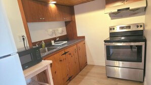 A kitchen with wooden cabinets, a built-in microwave, a stainless steel oven, and a wooden shelf unit. - Cozy Retro Suite with Garden Walkout, Games & Lounge! (Toronto)