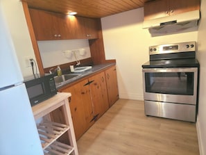 A kitchen with wooden cabinets, a built-in microwave, a stainless steel oven, and a wooden shelf unit.