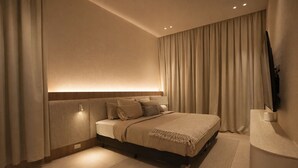 Ein modernes Hotelzimmer mit Bett, Vorhängen, einem Flachbildfernseher und einem Nachttisch.
