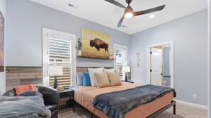 Ein Schlafzimmer mit Bett, Schreibtisch, Stuhl, Deckenventilator und einer Tür.
