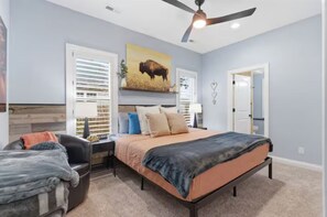 A bedroom with a bed, a desk, a chair, a ceiling fan, and a door. - WyNot! Monument House (Rapid City)