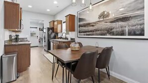 Eine moderne Küche mit Holzausstattung, einem Esstisch mit Stühlen und einem großen Landschaftsbild an der Wand.