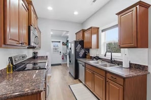 A modern kitchen with granite countertops, wooden cabinets, stainless steel appliances, and a large window. - WyNot! Monument House (Rapid City)