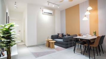 A modern living room with a sofa, a dining table with chairs, a small side table, and a potted plant.