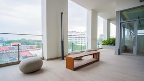 Ein großzügiger Balkon mit einer hölzernen Bank, einer hohen Stehlampe und einer Glastür, die auf einen mit Pflanzen bepflanzten Balkon führt.