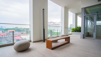 Un balcon spacieux avec un banc en bois, un grand lampadaire et une porte vitrée donnant sur un autre balcon agrémenté de plantes.