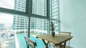 A balcony with a wooden table, a potted plant, and a view of a cityscape through large windows. - Dorsett Waterfront Subang by Guestonic (Subang Jaya)